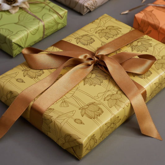 Gift box with floral pattern, yellow background and brown ribbon on a gray surface